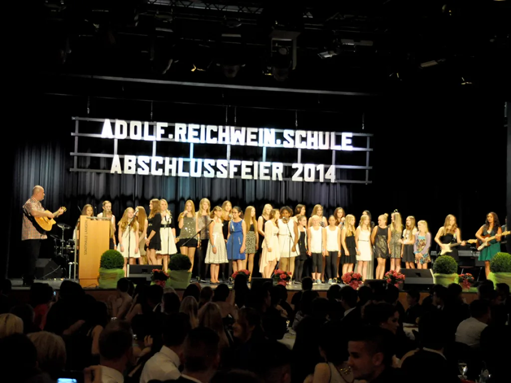 Große Gruppe steht bei der Zeugnisübergabe auf der Bühne.